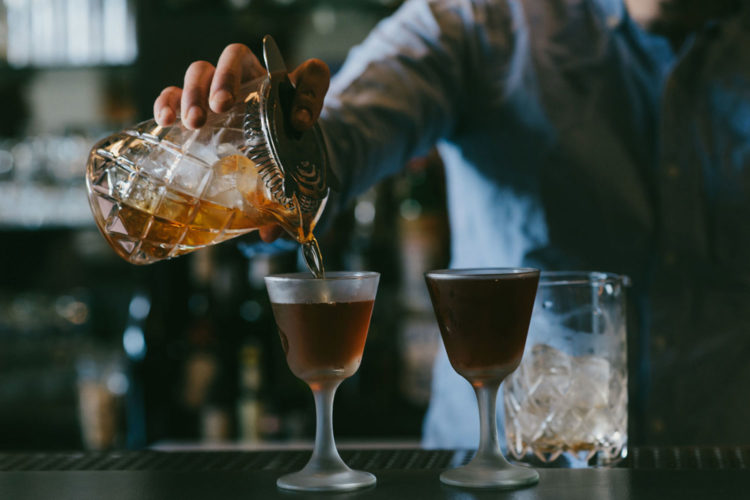 bartender pouring mixed cocktail into two glasses