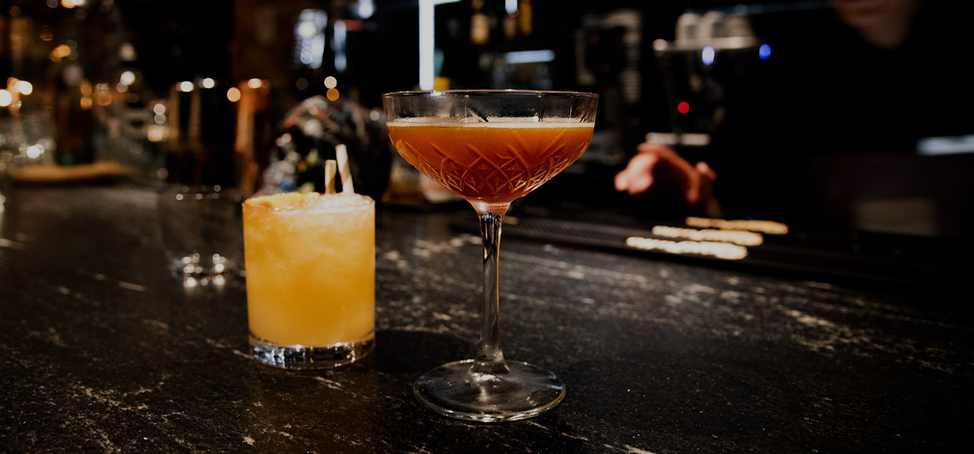 cocktail in long stemmed glass next to shorter drink on bar table