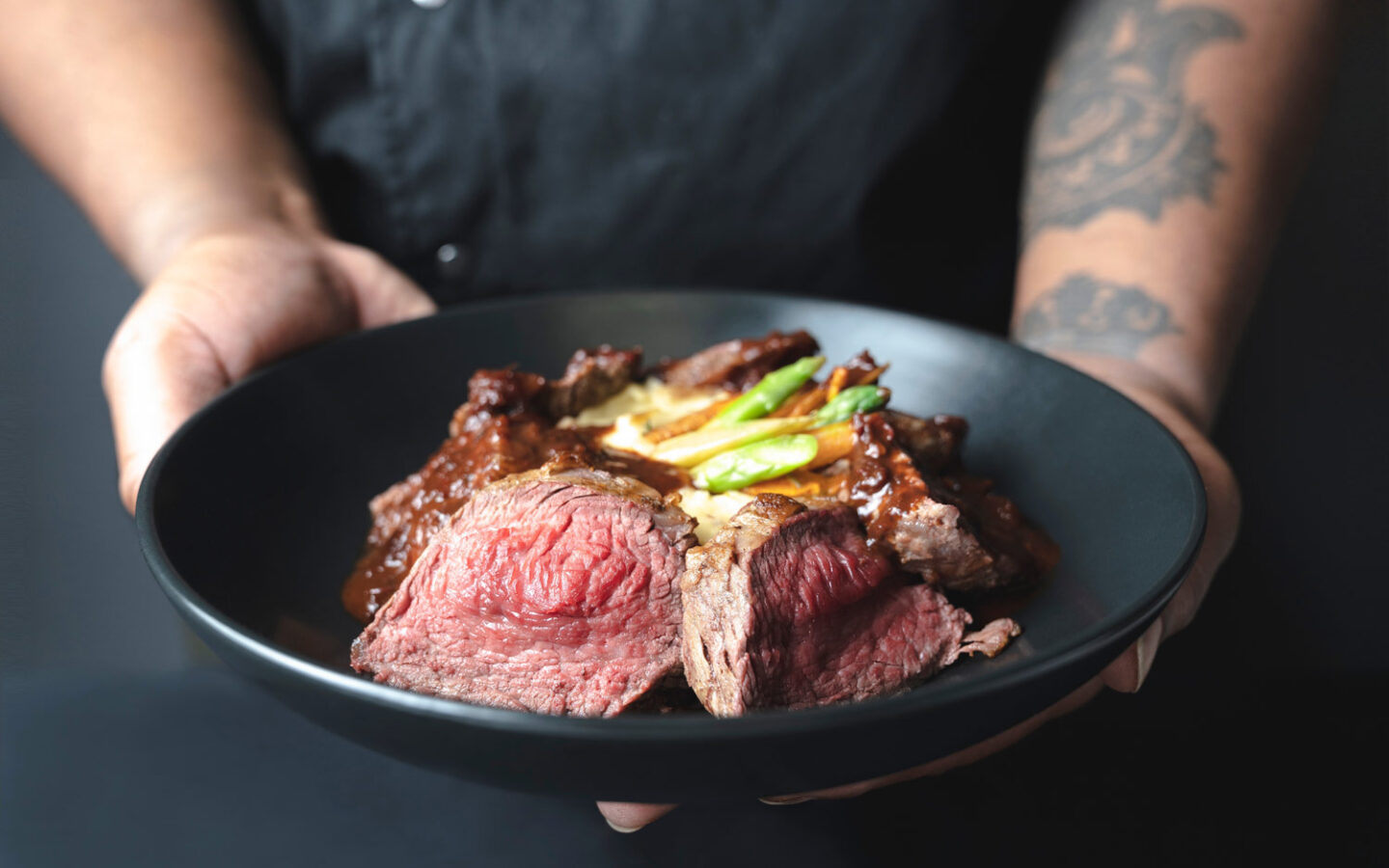 A server holding out a plate of sliced rare beef