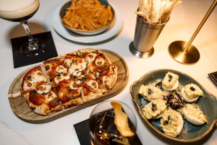 Pizza, pasta, and appetizers served with cocktails on a table.