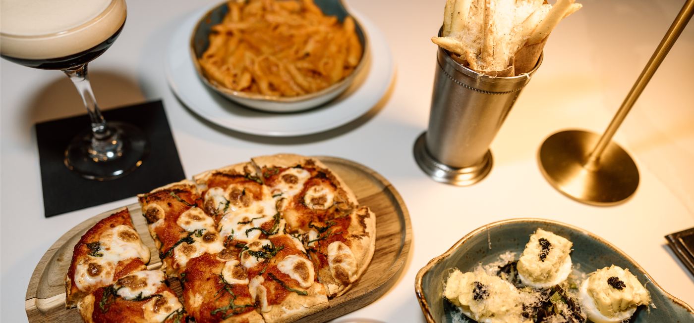 Pizza, pasta, and appetizers served with cocktails on a table.