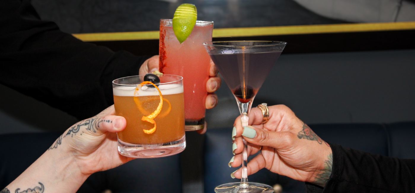Three cocktails being toasted at a lounge table.