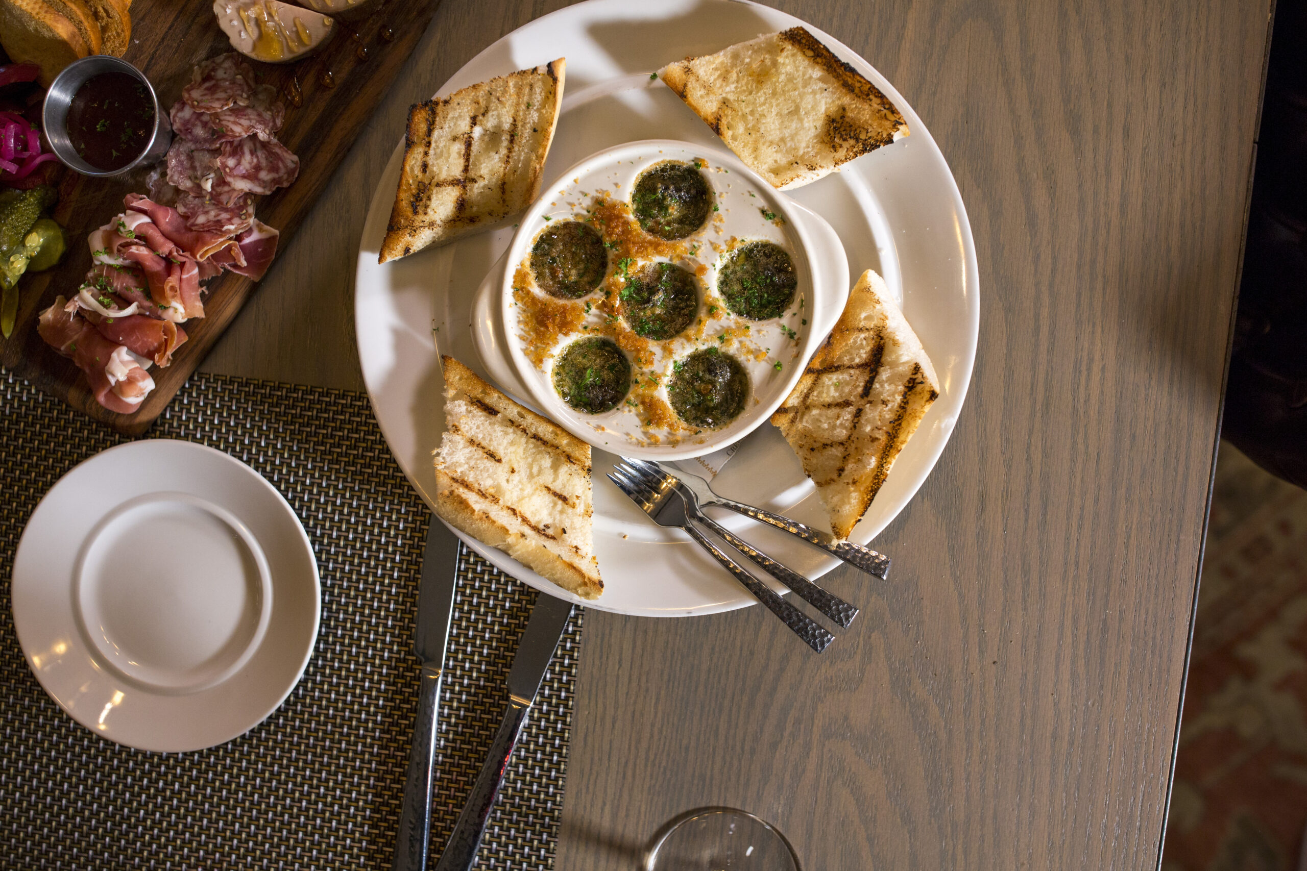 large white plate with bread and escargot on it with a platter of lunch meats next to it