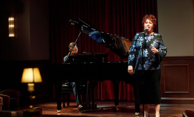 woman singing into microphone while man plays grand piano