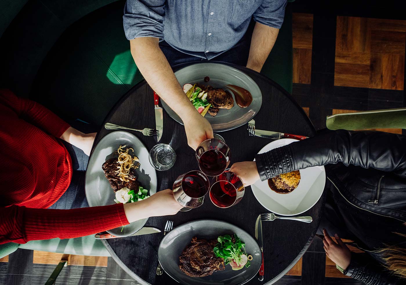 people clinking their wine glasses over their entree dishes