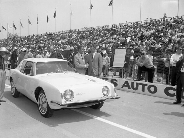 old racing car on track with crowded stands in background