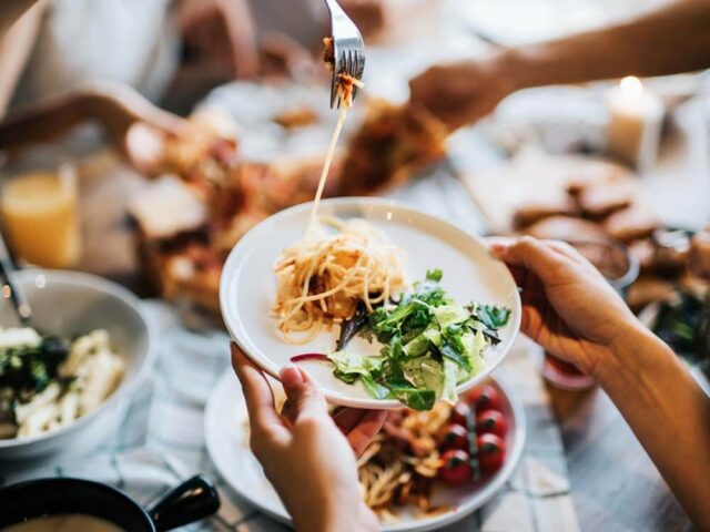 a pair of hands picking up a plate holding a noodle dish