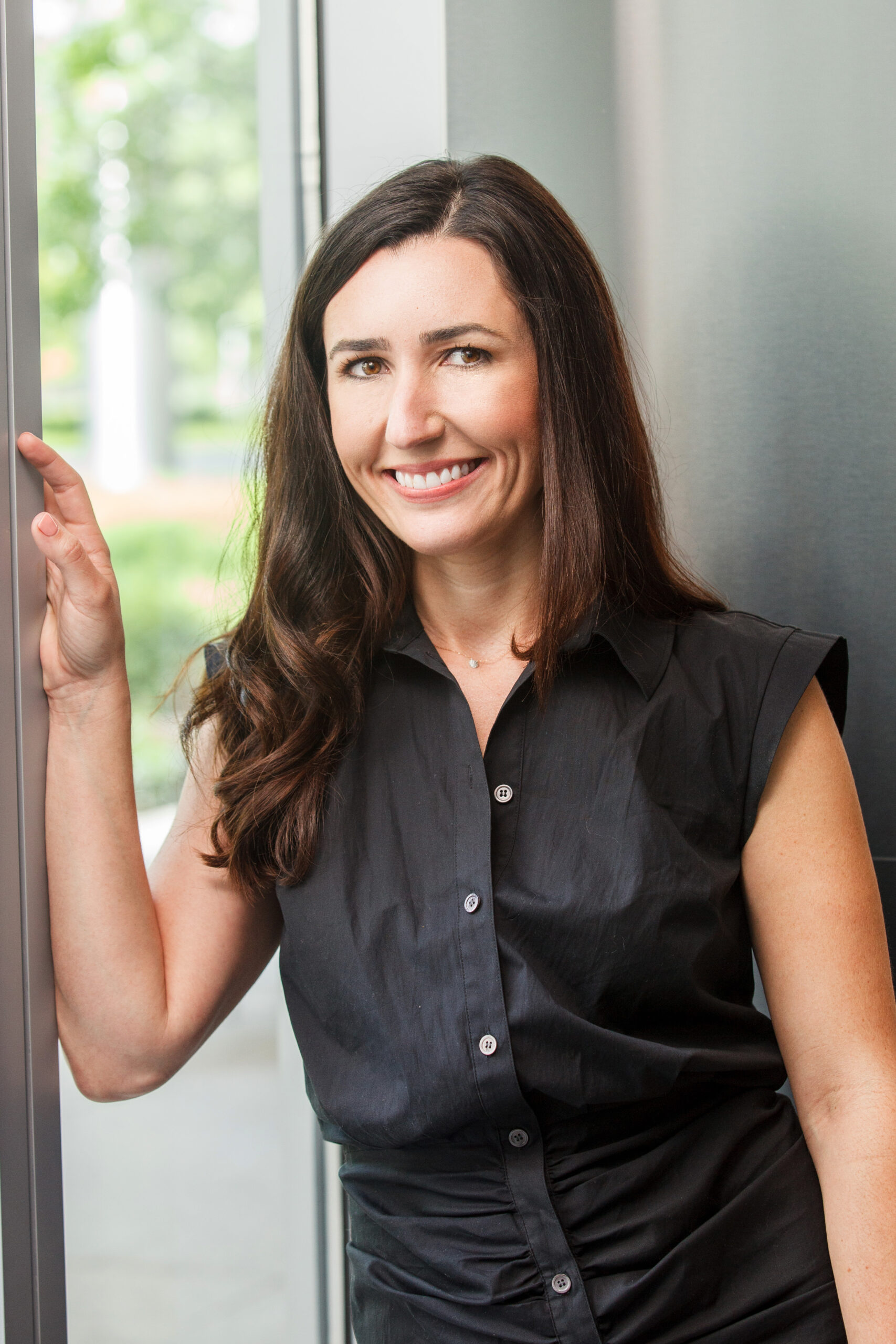 smiling brunette woman in black short-sleeve shirt leaning against window frame