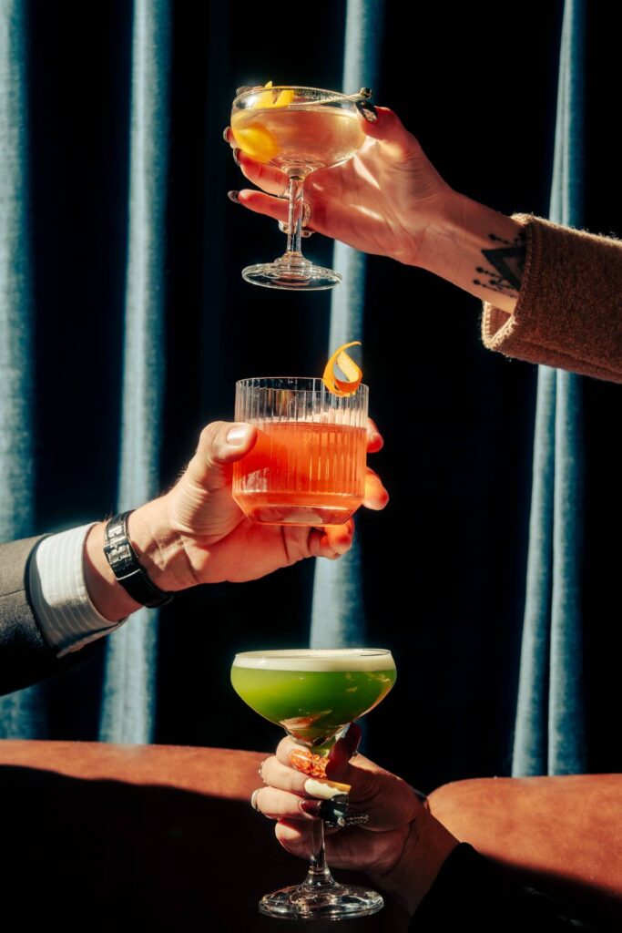 three people holding out cocktails in various shaped glasses