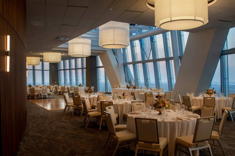 meeting space with many set tables surrounded by chairs lit by large circular lighting fixtures
