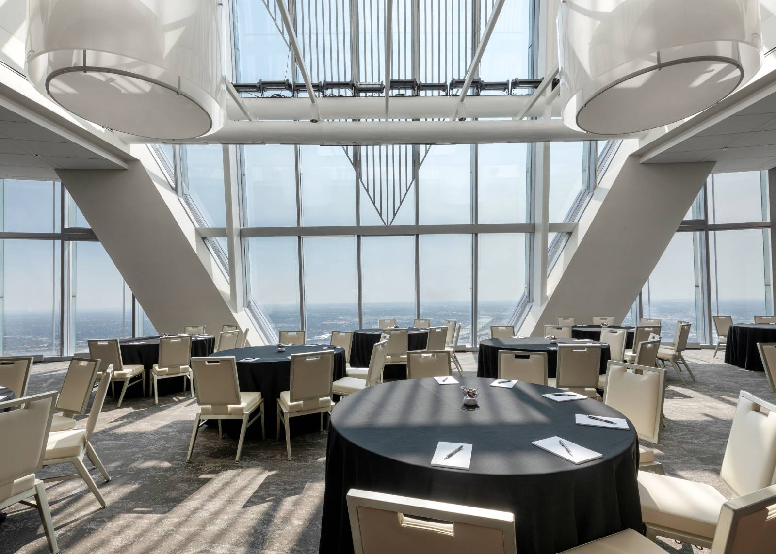 Bright modern event space with round tables, floor-to-ceiling windows, and panoramic city views.