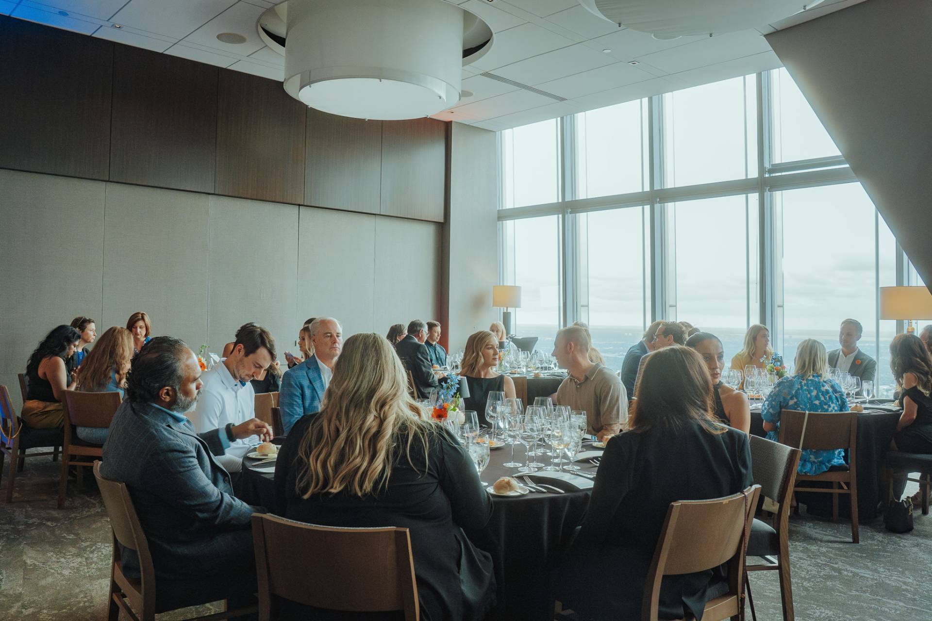 Guests seated at round tables enjoying a dinner event near large windows with a scenic view.