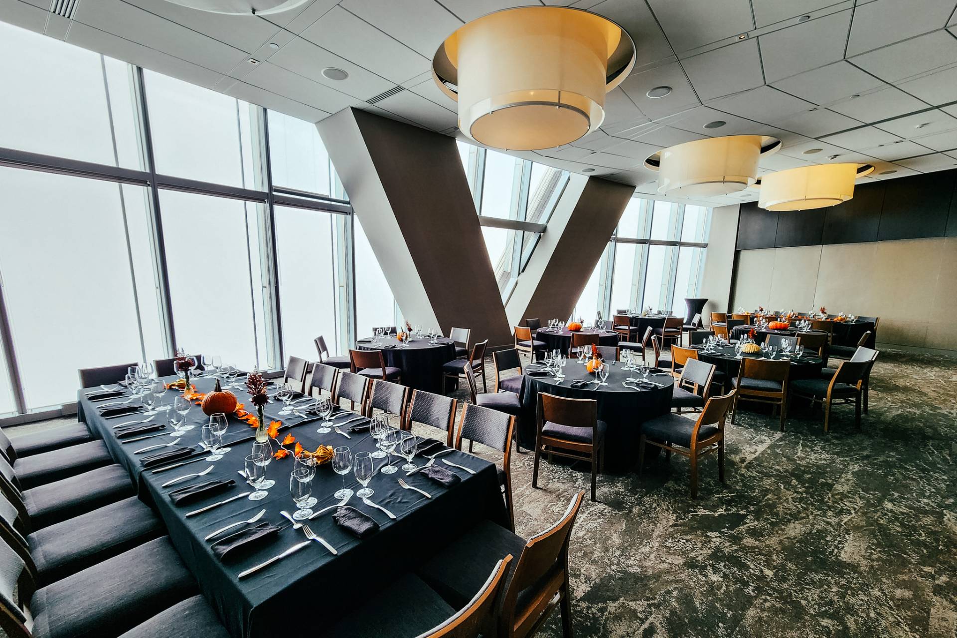 Modern private dining room with floor-to-ceiling windows, black table settings, and autumn-themed decorations.